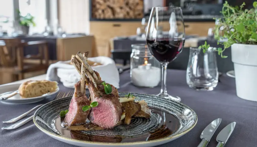 Carré d'agnello al forno con funghi e un bicchiere di vino rosso, un abbinamento perfetto per un pasto speciale.
