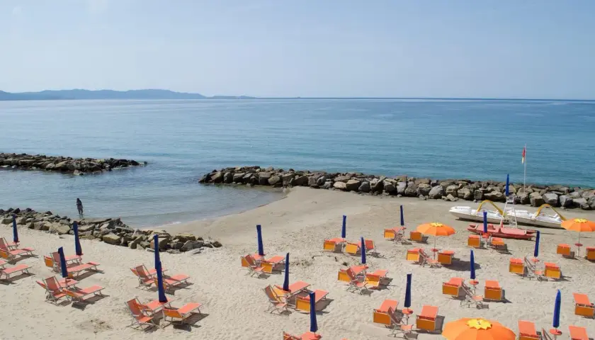 Spiaggia attrezzata con lettini e ombrelloni arancioni, mare azzurro e scogli. Un sogno di vacanza a Pratoranieri Follonica.