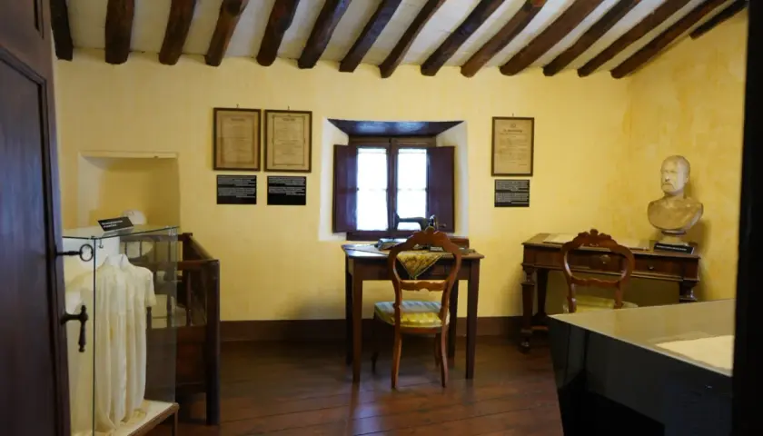 Interno di una casa museo, con travi a vista, una scrivania con macchina da cucire, un busto e un abito in esposizione. Un luogo dove le case della memoria prendono vita.