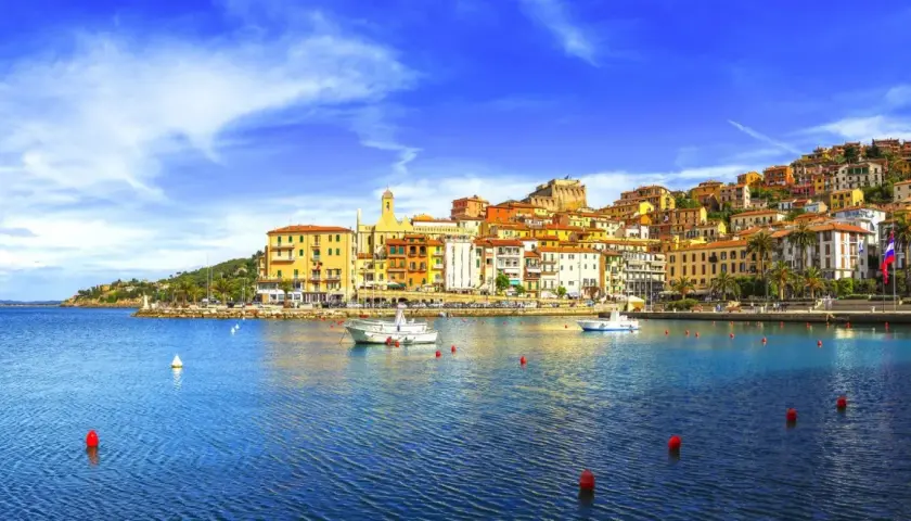 Vista del porto di Porto Santo Stefano, con case colorate che si arrampicano sulla collina e barche sull'acqua blu.