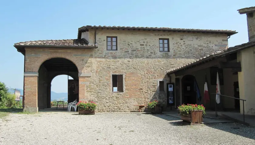 La casa di Giotto, un edificio in pietra con un grande arco, fiori rossi e bandiere.