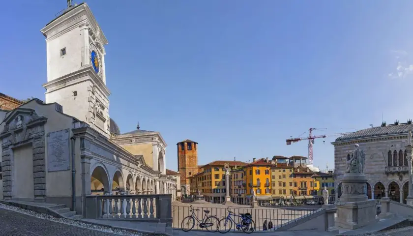 La piazza della Libertà, con la sua torre dell'orologio, edifici colorati e due biciclette in primo piano, sotto un cielo azzurro.