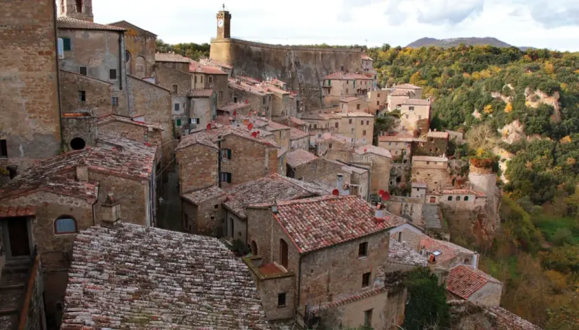 Sorano, Toscana: un borgo medievale arroccato su una rupe tufacea, con tetti rossi e case in pietra che si fondono con il paesaggio autunnale.