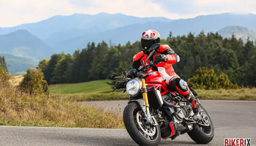Motociclista in tuta rossa affronta una curva sul passo del giogo, con montagne sullo sfondo.