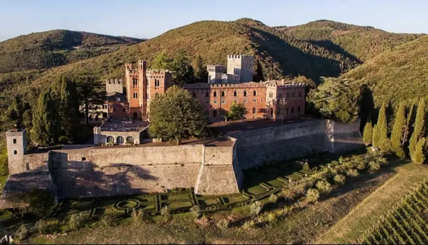 Il Castello di Brolio, imponente fortezza in mattoni rossi, domina le colline toscane, circondato da vigneti e cipressi.