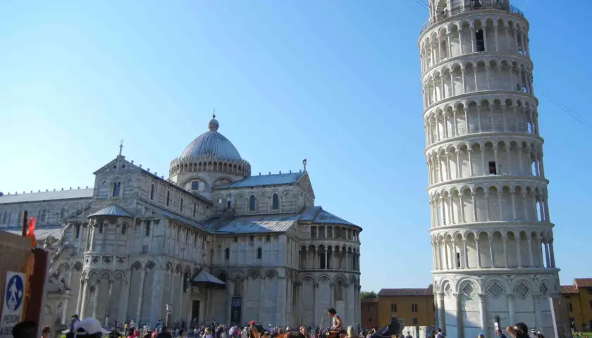 Visitare Pisa: la Torre Pendente e il Duomo svettano sotto un cielo azzurro, mentre turisti e una carrozza trainata da cavalli animano la piazza.