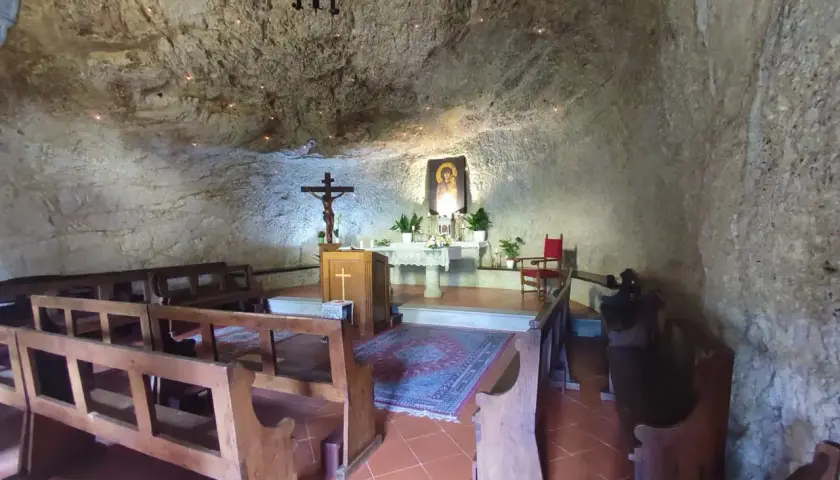 Interno dell'eremo di Calomini, con panche in legno, altare, crocifisso e un'icona sacra incastonati nella roccia.
