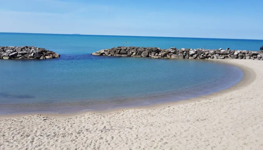 Spiaggia di Marina di Pisa con acque calme e dighe frangiflutti in pietra.