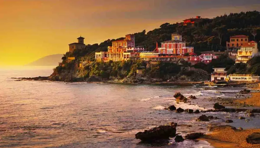 Ville colorate aggrappate alla scogliera, con il mare che lambisce la costa rocciosa. Un tramonto dorato illumina i borghi vicino Castiglioncello.