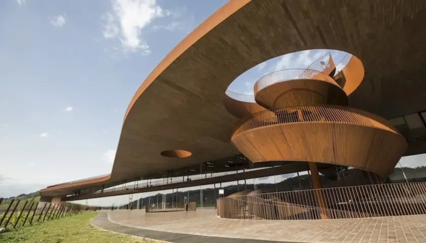 Edificio moderno con scala a chiocciola in legno, probabile la **best winery in Tuscany**, immersa nel verde.