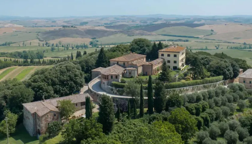 Un borgo toscano con casali in pietra e un edificio giallo, immerso nel verde e con dolci colline sullo sfondo. Castelnuovo Tancredi, un'oasi di pace.