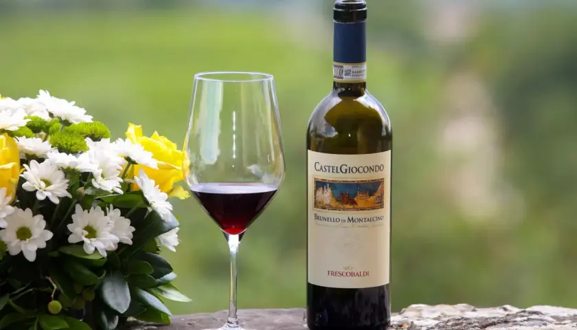 Un bicchiere di Brunello di Montalcino, un vino pregiato, accanto a un bouquet di fiori e una bottiglia CastelGiocondo.