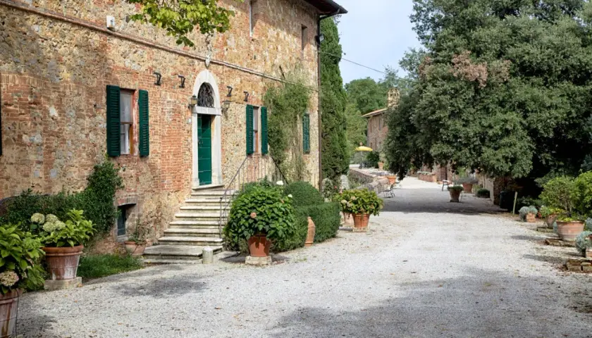 Ingresso della fattoria del colle Trequanda, con scalinata in pietra, porta verde e piante in vaso.