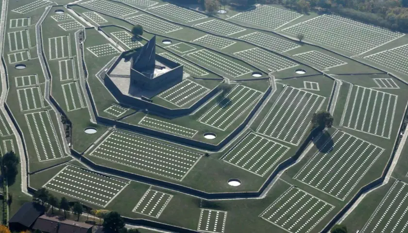 Vasta distesa di tombe bianche disposte in file ordinate, con un imponente monumento centrale. Il cimitero tedesco del Passo della Futa, un luogo di memoria.