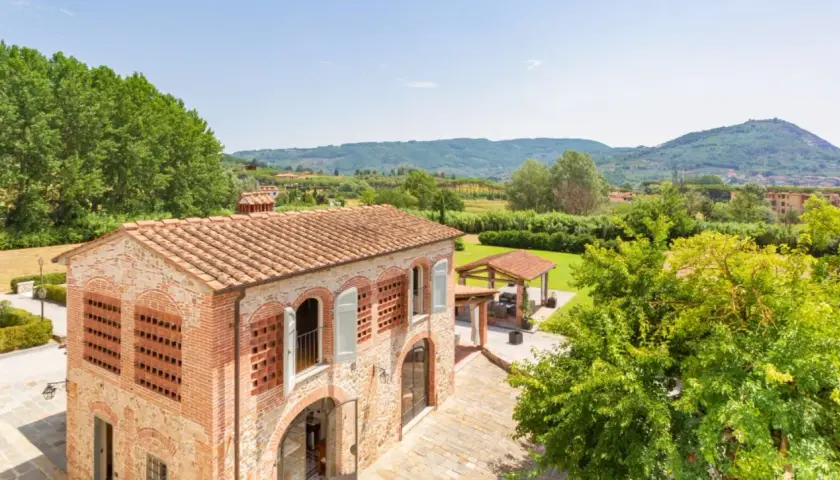 Antica pieve a Nievole con tetto in cotto, circondata da verde lussureggiante e colline toscane.