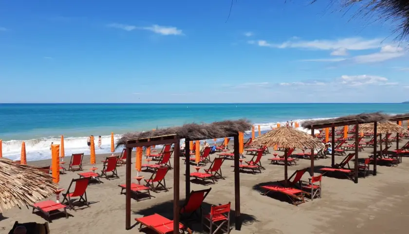 Marina di Bibbona spiagge più belle: lettini rossi e ombrelloni di paglia sotto un cielo azzurro, con il mare calmo all'orizzonte.