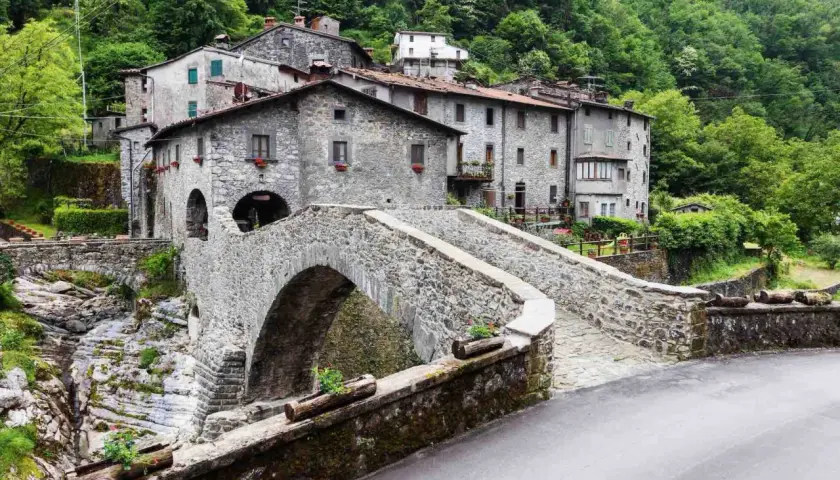 Ponte in pietra a Vergemoli, con case in pietra e vegetazione lussureggiante sullo sfondo. Le fabbriche di Vergemoli sembrano immerse nella natura.