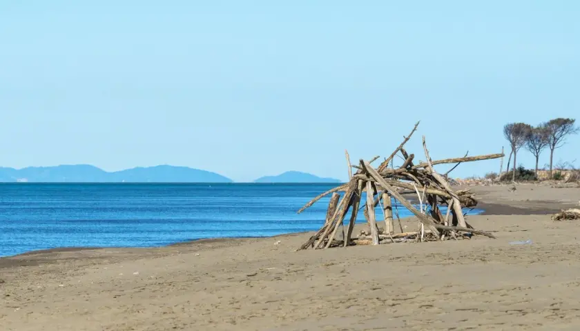 Spiaggia del Parco dell'Uccellina con un rifugio di legni sulla sabbia e il mare blu all'orizzonte.