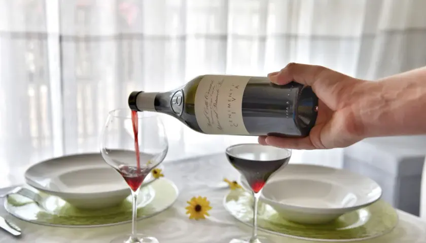 Versare vino rosso in un calice, un passo fondamentale per capire come si fa il vino rosso. La tavola è apparecchiata.