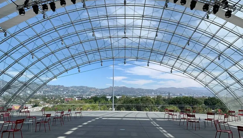 Spazi all'aperto del museo de la academia, con sedie rosse disposte e vista sulle colline di Los Angeles sotto una struttura a volta in vetro.