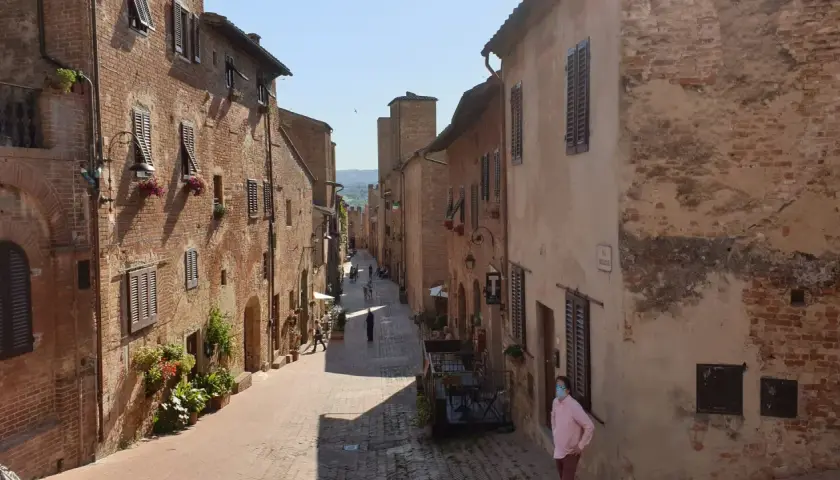 Un vicolo medievale a Certaldo, dove si trova il borgo antico con case in mattoni, finestre con persiane e fiori.