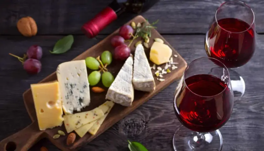 Un tagliere di formaggi misti, uva e frutta secca, perfetto per i rosso di Montalcino abbinamenti. Due calici di vino rosso completano la scena.