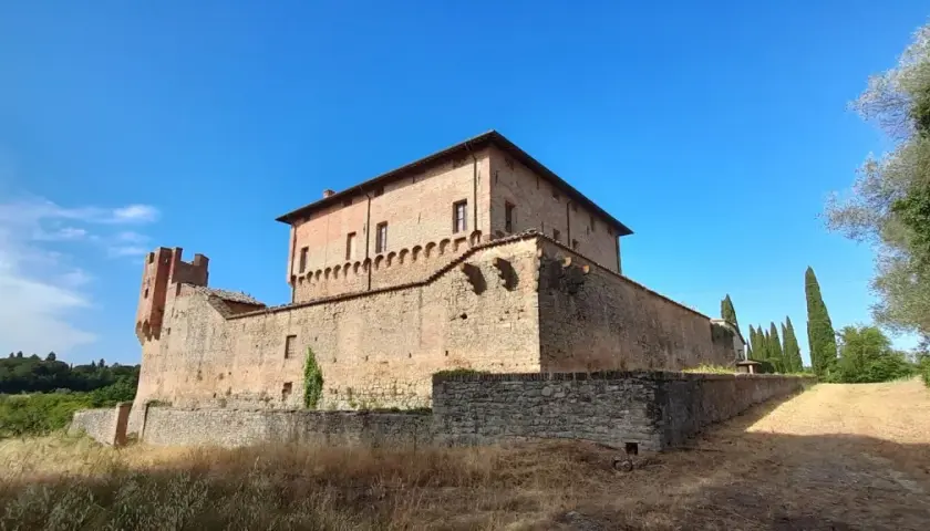 Rocche e mura antiche a Civitella Paganico cosa vedere: un castello medievale in mattoni rossi sotto un cielo azzurro, circondato da vegetazione rigogliosa.