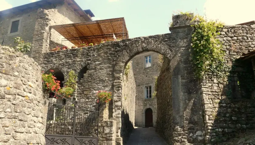 Un vicolo suggestivo a Casola in Lunigiana, con un arco in pietra, fiori rossi e edera rampicante.