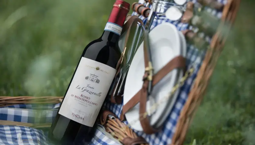 Cesto da picnic con bottiglia di vino rosso, probabilmente da uve sangiovese, e piatti.