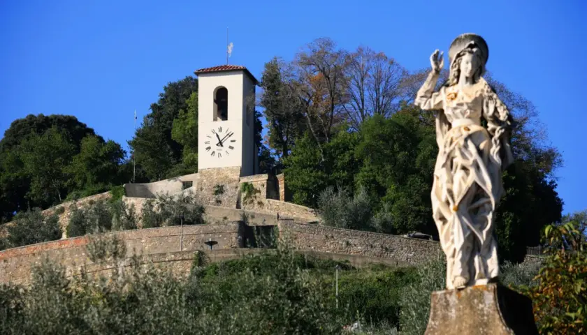 Statua di santo e torre dell'orologio su una collina verdeggiante, un'immagine che cattura l'essenza di cosa vedere ad Artimino.