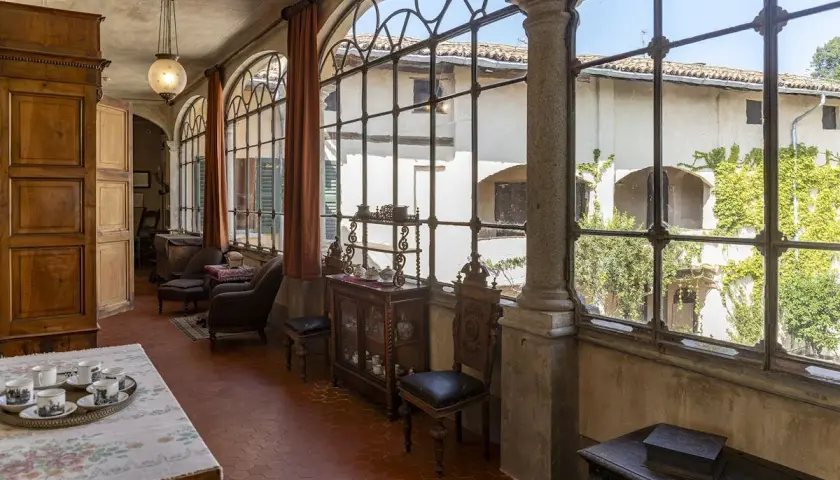 Interno elegante della villa Macchi con mobili d'epoca, grandi finestre ad arco e vista sul cortile verdeggiante.
