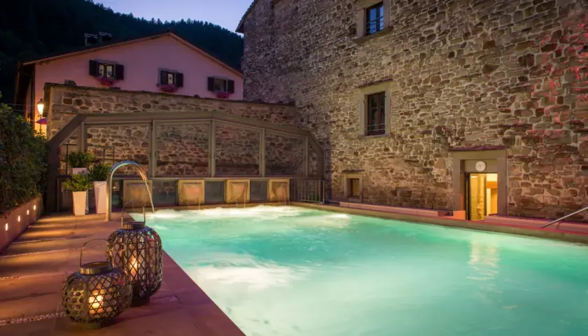 Piscina termale illuminata di notte, con cascate d'acqua e lanterne decorative. Un'oasi di relax nelle terme vicino Arezzo.