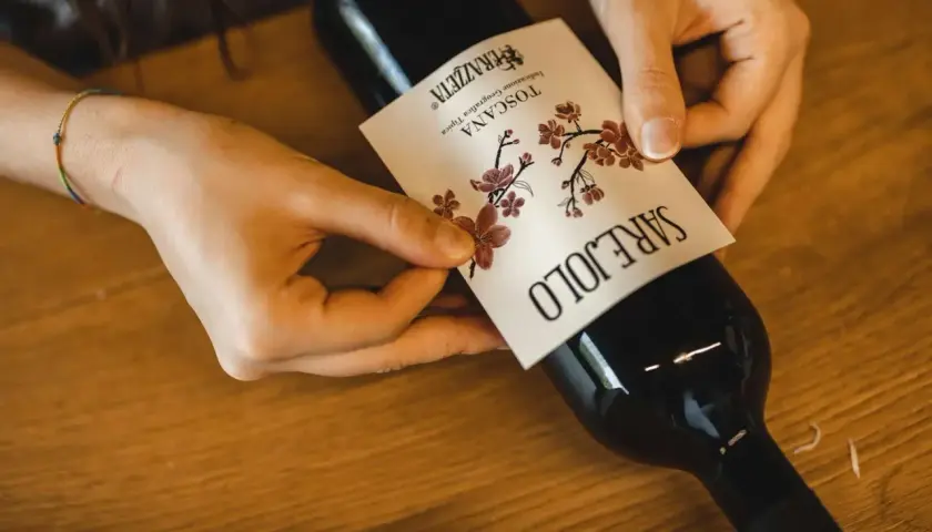 Mani che applicano l'etichetta a una bottiglia di vino rosso, forse il best wine in Tuscany.