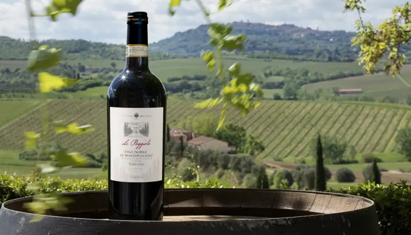 Bottiglia di Vino Nobile di Montepulciano su un barile, con sullo sfondo le dolci colline toscane e i loro vigneti.