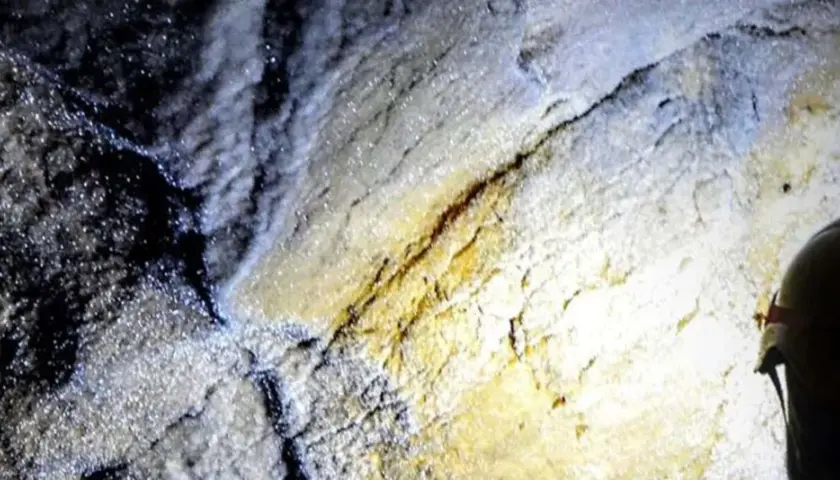 Esplorazione della grotta turistica Antro del Corchia: rocce scintillanti e un casco illuminato da una torcia.