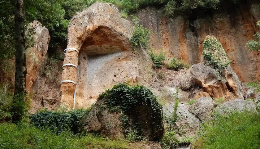 Antica tomba etrusca scavata nella roccia, con un pilastro decorato da fasce metalliche, immersa nel verde della necropoli di Sovana.