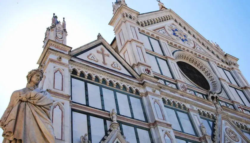 Statua di un poeta toscano davanti alla facciata in marmo di una chiesa fiorentina.