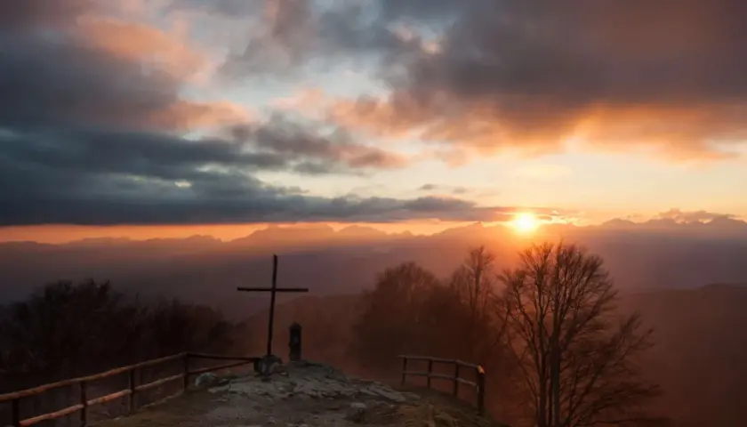Croce in cima a una collina al tramonto, con montagne sullo sfondo. Un luogo suggestivo a San Pellegrino in Alpe.