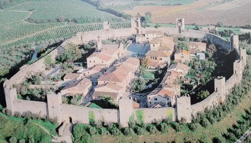 Vista aerea di Monteriggioni, un borgo medievale fortificato in Toscana, con le sue mura intatte e le torri che si stagliano sul paesaggio collinare.