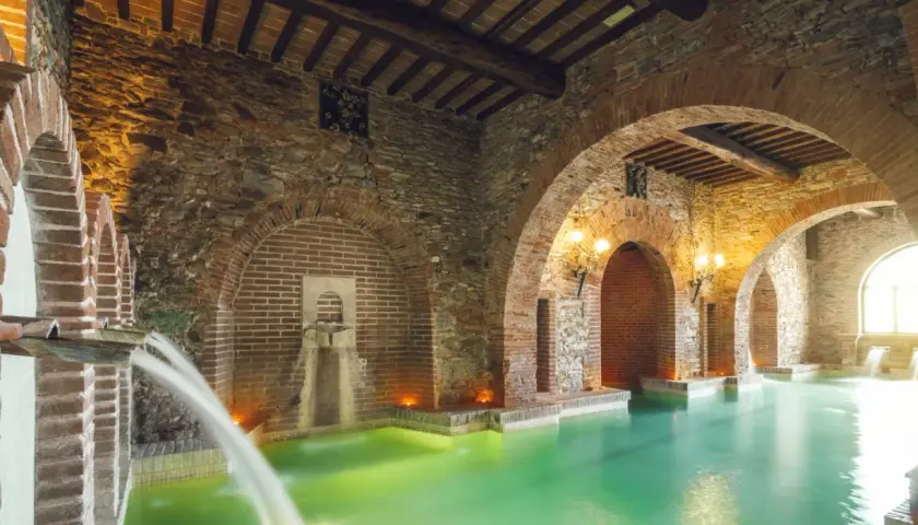Piscina termale con archi in mattoni e pietra, cascate d'acqua e luci soffuse, un'oasi di relax nel paese di Venturina Terme.
