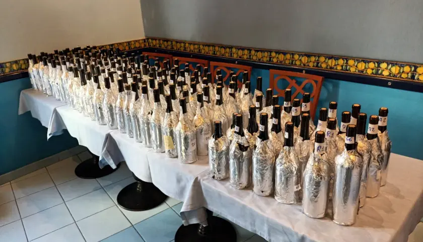 Many wine bottles wrapped in foil, lined up on a table for a tasting.