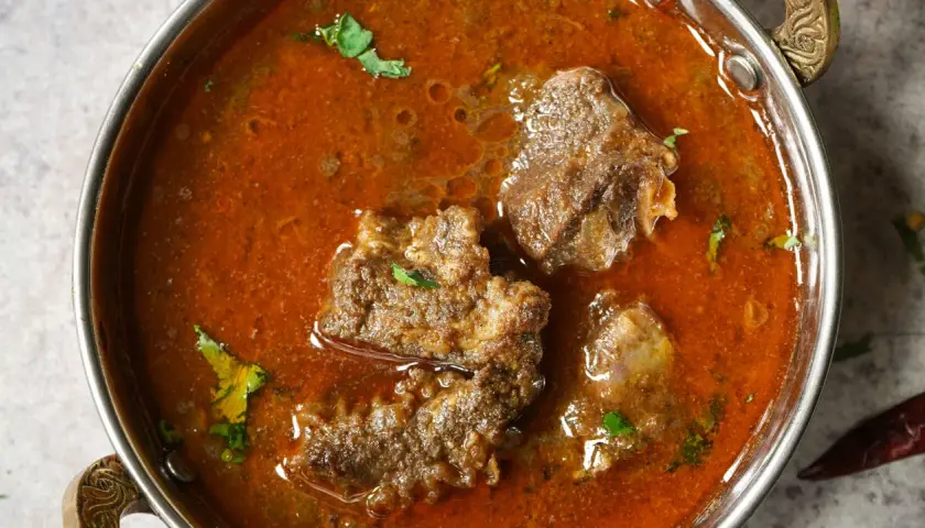 Un invitante buglione di agnello in una ciotola metallica, con pezzi di carne tenera immersi in un ricco sugo speziato e guarnito con erbe fresche.