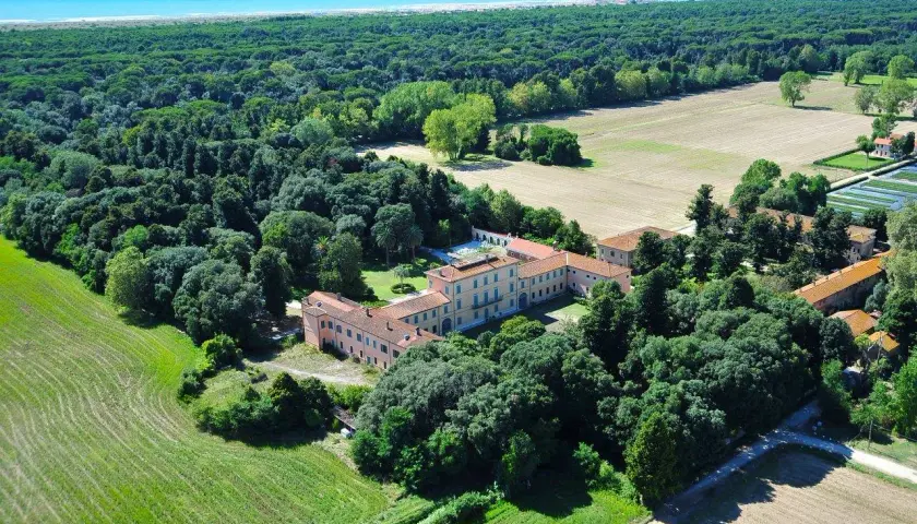 Villa storica immersa nella pineta di levante, con campi coltivati e il mare all'orizzonte.