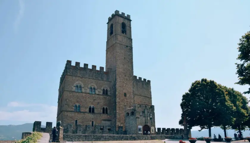 Un antico borgo alla collina domina il paesaggio, con un imponente torrione che svetta verso il cielo azzurro.
