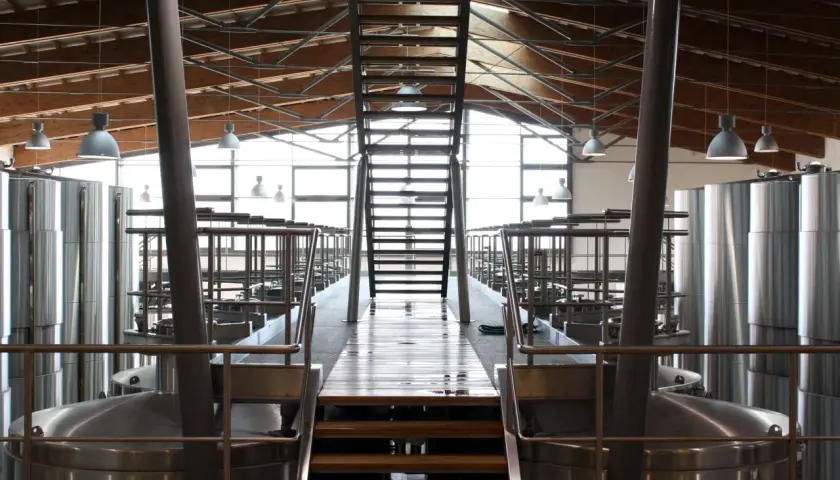 Interno di una cantina moderna con grandi serbatoi d'acciaio e una scala centrale. L'architettura ricorda un progetto di Renzo Cotarella.