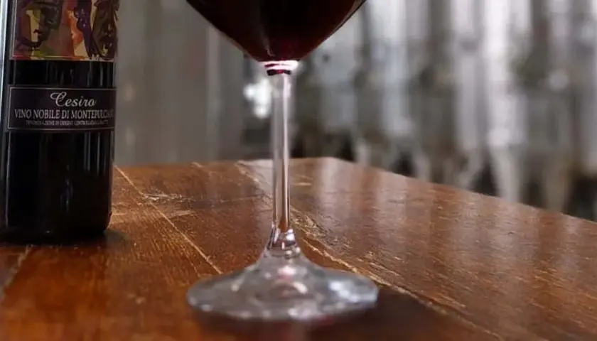Bottiglie di Vino Nobile di Montepulciano e un calice di rosso, in un'ambientazione che evoca le cantine delle province di Siena.