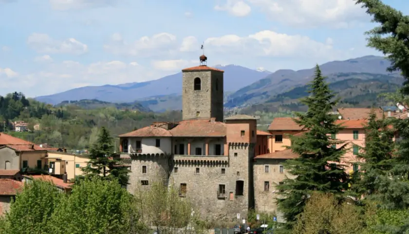 La Rocca Ariostesca domina il borgo con la sua torre imponente, circondata da colline verdi e un cielo azzurro con nuvole bianche.