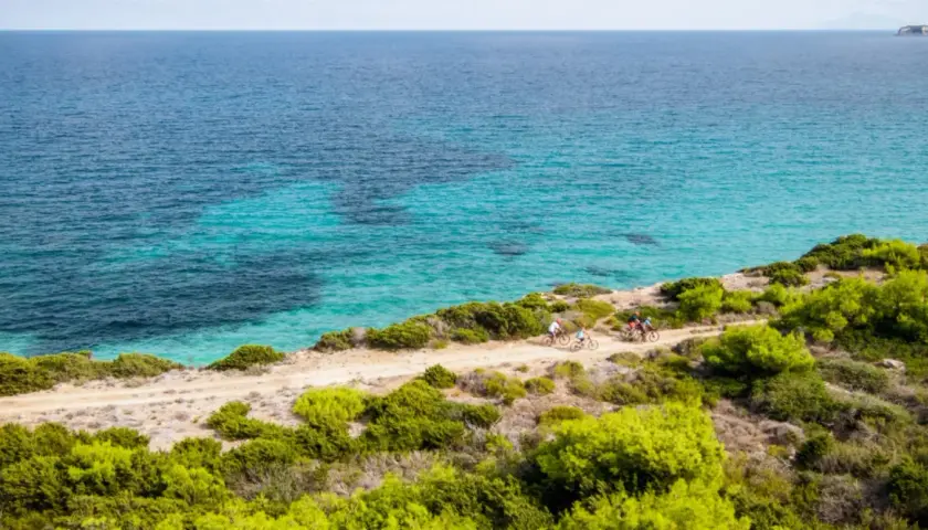 Ciclisti esplorano la costa dell'isola di Pianosa, con acque cristalline e vegetazione mediterranea.