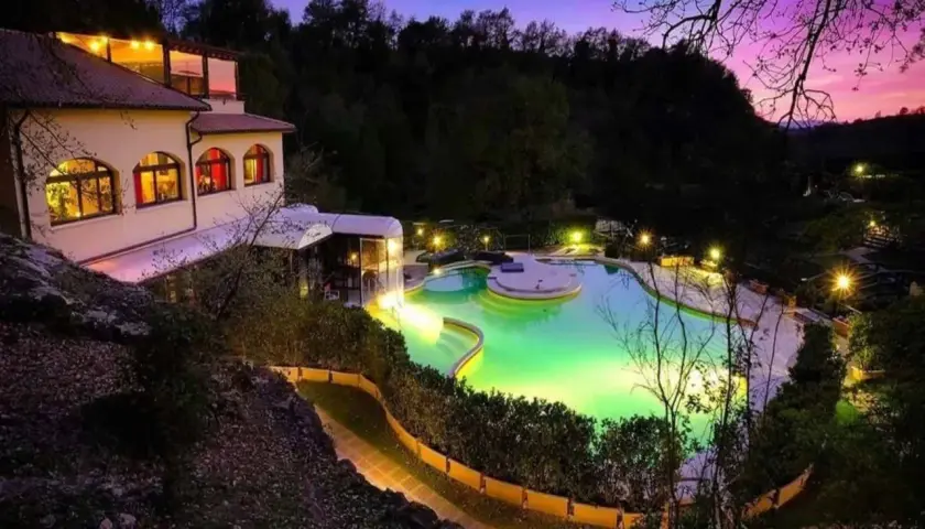 Piscina illuminata e un edificio a San Carlo Terme al tramonto, con cielo viola e rosa.