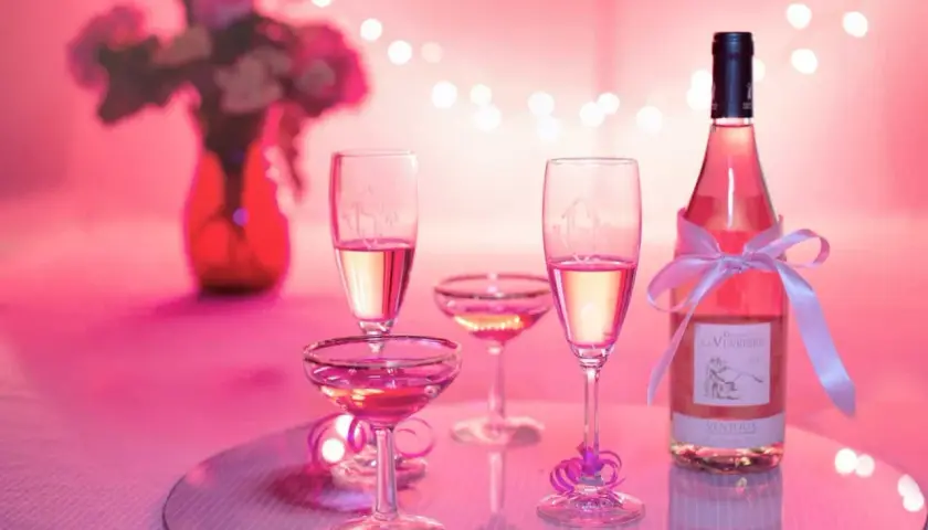 Bottiglia e calici di vino rosato, un brindisi alla vinificazione in rosato, con fiori e luci soffuse.